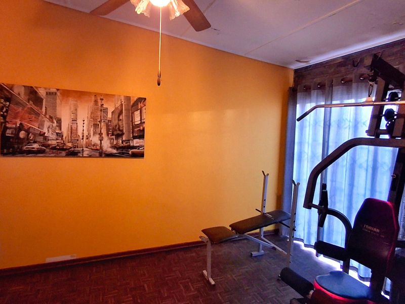 A dedicated gym space featuring parquet flooring, a ceiling fan, and sliding glass doors providing natural light.