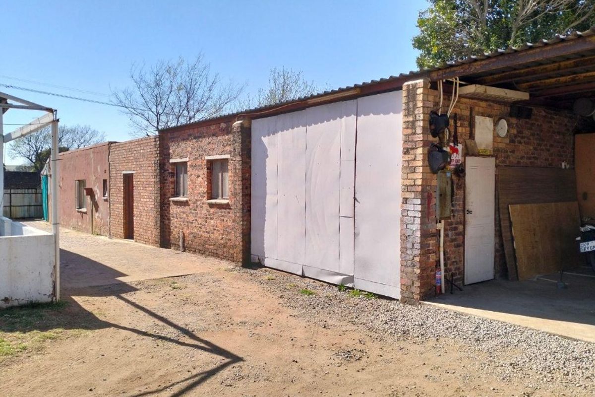 Rear exterior view of the property featuring a brick structure with a covered carport area and paved driveway access.