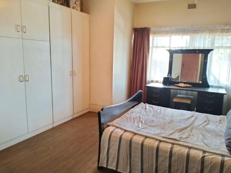 A bedroom featuring built-in cupboards, timber flooring, and a large window allowing natural light.