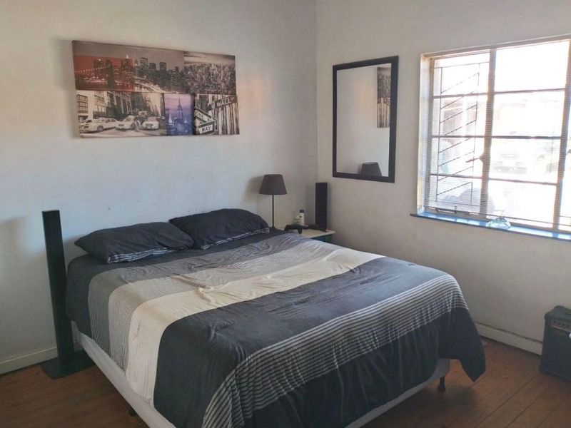 A bedroom featuring timber flooring and a window with security bars, requiring minor cosmetic updates to improve the overall finish.