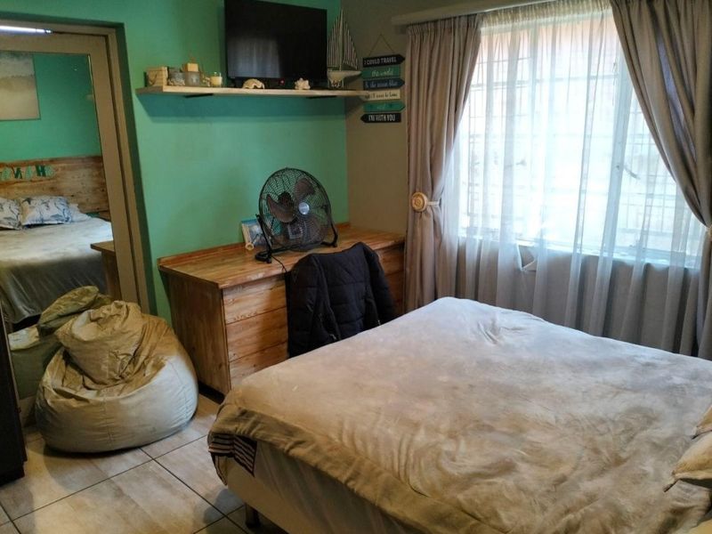 A bedroom featuring tiled flooring, built-in shelving, and a window with curtain tracks, providing a functional space with potential for modern updates.