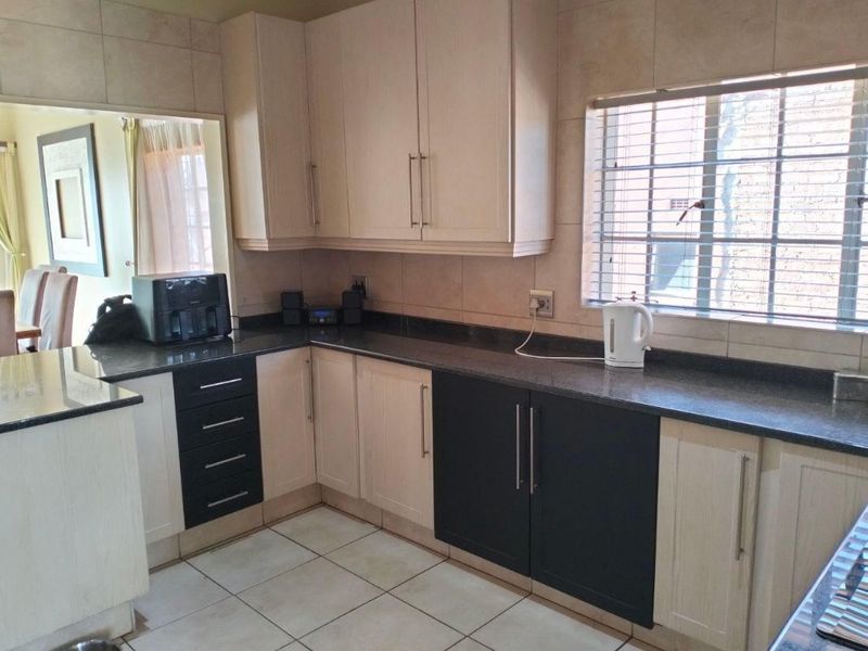 A functional kitchen featuring two-tone cabinetry, granite countertops, and tiled flooring, offering a practical layout with natural light from the side window.