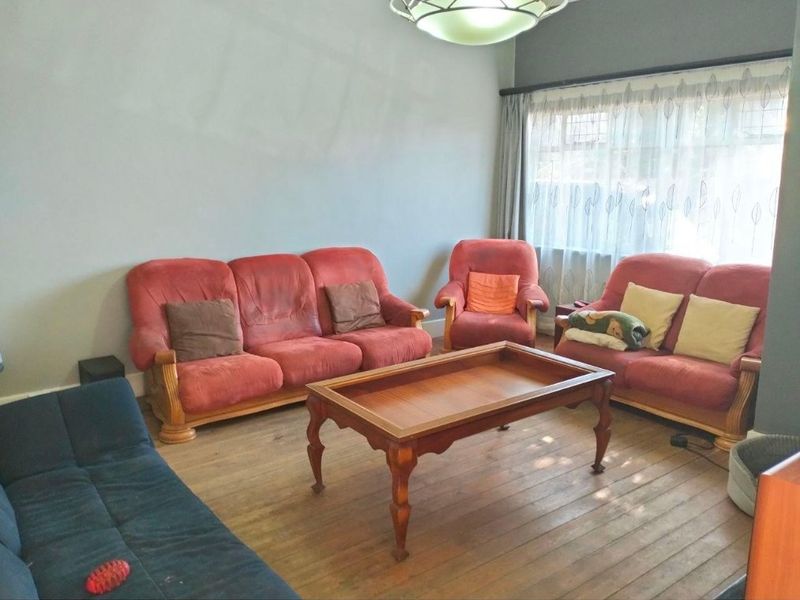 A living room featuring hardwood flooring, a large window with curtains, and a central ceiling light fixture.
