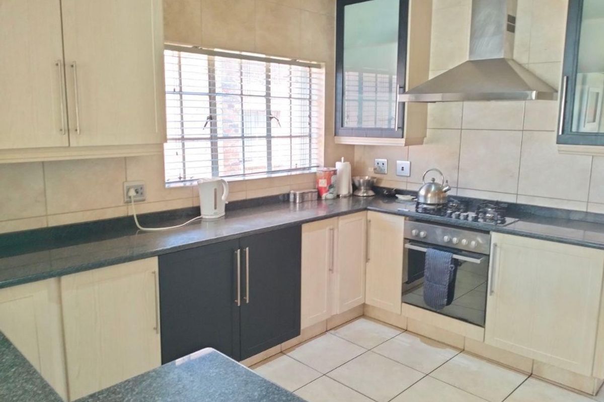 A functional kitchen featuring two-tone cabinetry, granite countertops, a gas hob, and a stainless steel extractor fan with tiled finishes throughout.