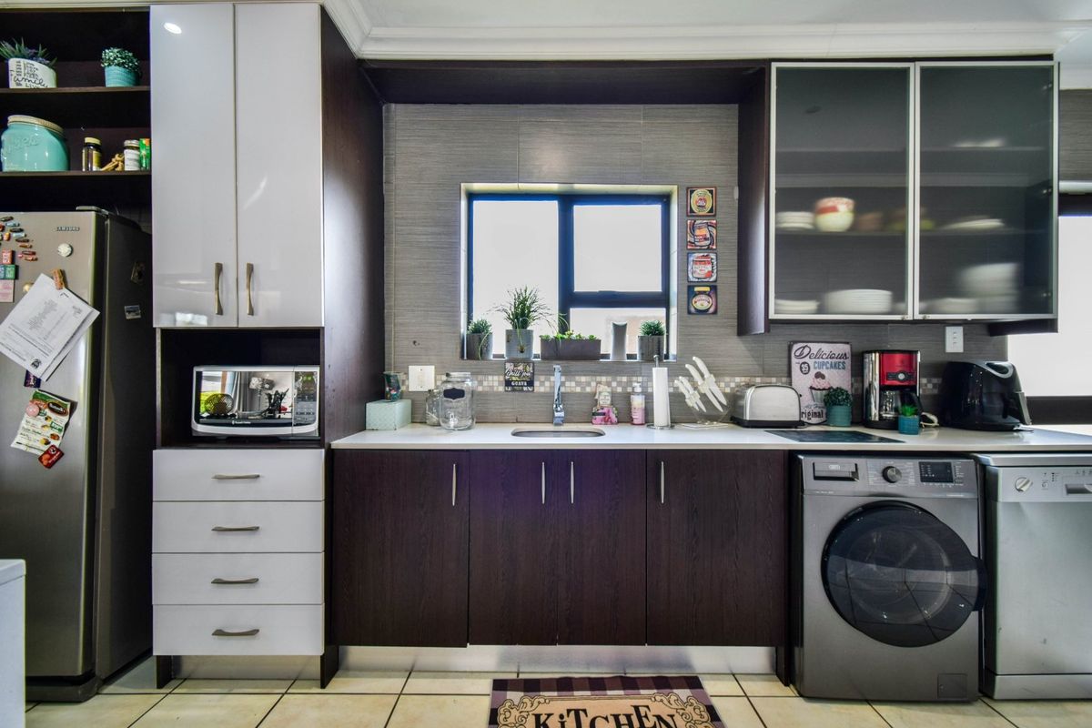 A functional kitchen featuring dark wood and white cabinetry, tiled backsplash, integrated laundry appliances, and ample storage space with a central window.