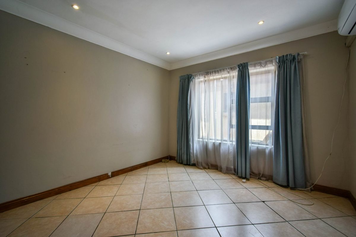 A spacious, empty bedroom featuring neutral wall tones, tiled flooring, recessed downlighting, and a wall-mounted air conditioning unit.