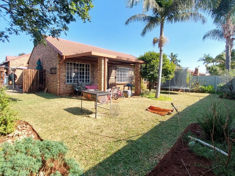Rear view of a brick townhouse featuring a covered patio, established garden, and secure perimeter fencing.