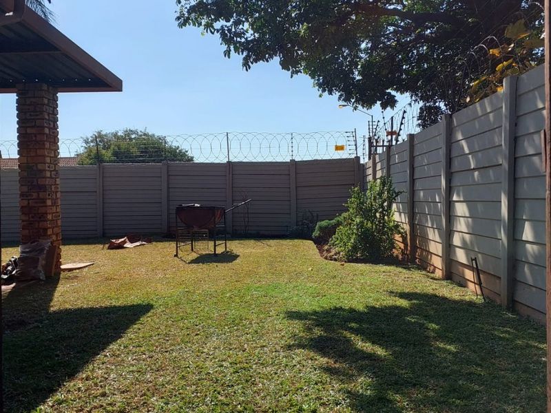 A private rear garden featuring a lawn, enclosed by precast concrete walling with security razor wire and a covered patio area.