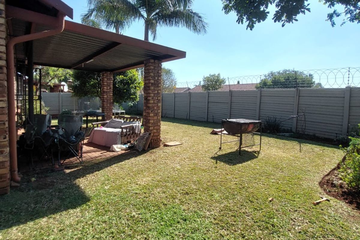 Rear garden featuring a covered patio with brick pillars, a lawn area, and a secure precast concrete boundary wall with razor wire.