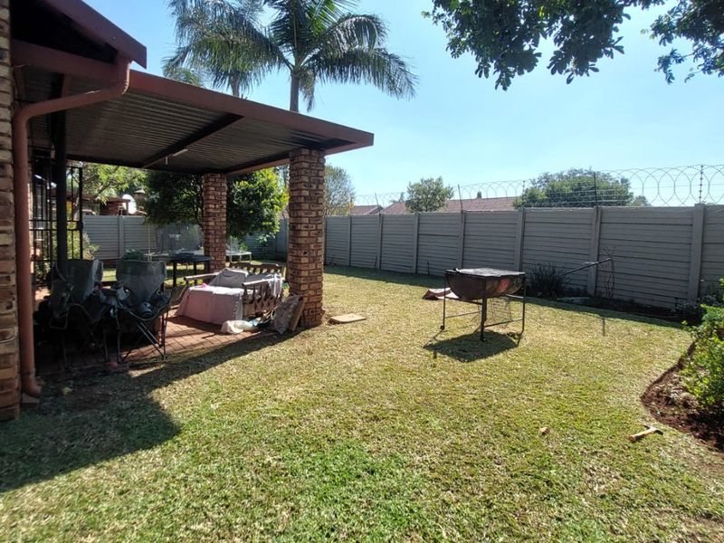 Rear garden featuring a covered patio with brick pillars, a lawn area, and a secure precast concrete boundary wall with razor wire.