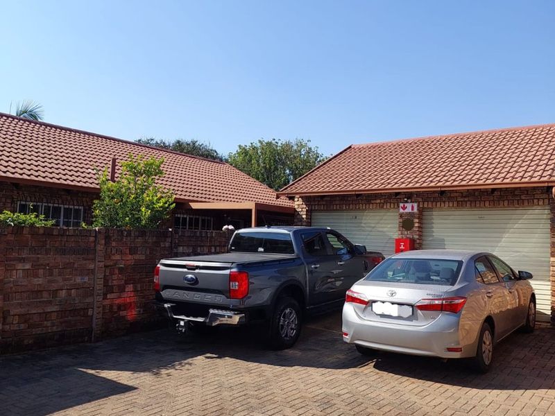Front exterior view of the townhouse featuring a paved driveway, face brick boundary wall, and a double garage with tiled roofing.