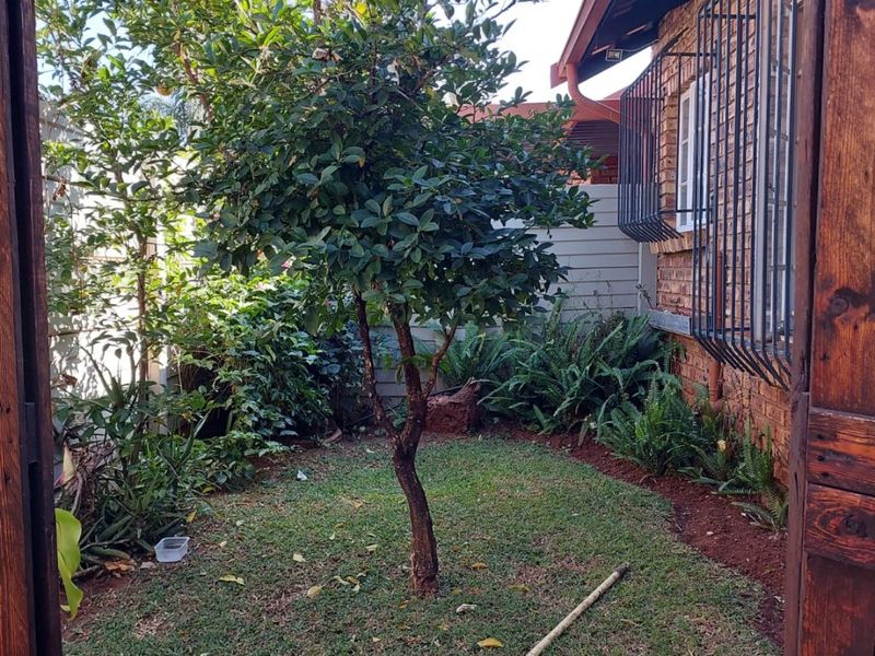 A view of the rear garden area featuring a small lawn, established tree, and brick exterior wall with security bars on the window.