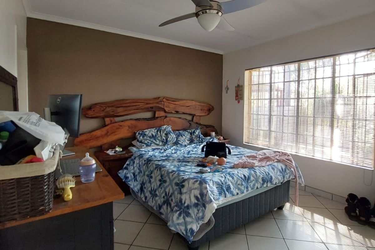 A bedroom featuring tiled flooring, a ceiling fan, and large windows with security bars, providing natural light.