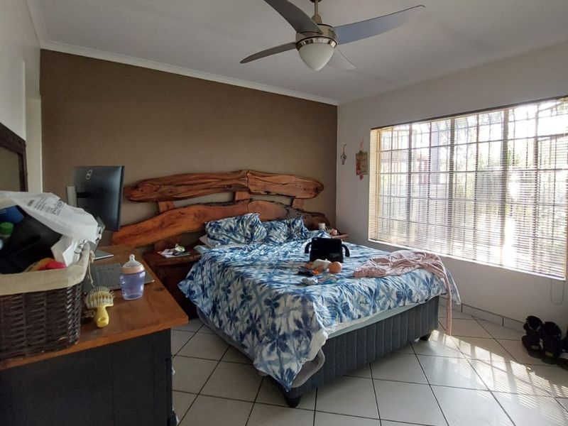 A bedroom featuring tiled flooring, a ceiling fan, and large windows with security bars, providing natural light.