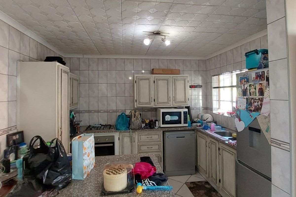 A functional kitchen featuring tiled walls and flooring, granite countertops, built-in cabinetry, and integrated appliances, offering potential for a modern renovation.
