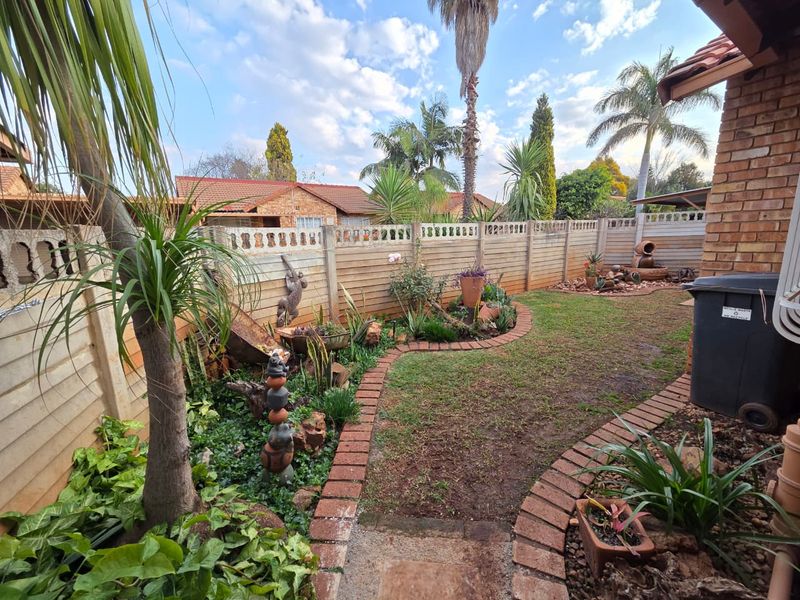 A private rear garden featuring a lawn area, established garden beds with brick edging, and a secure precast concrete boundary wall.