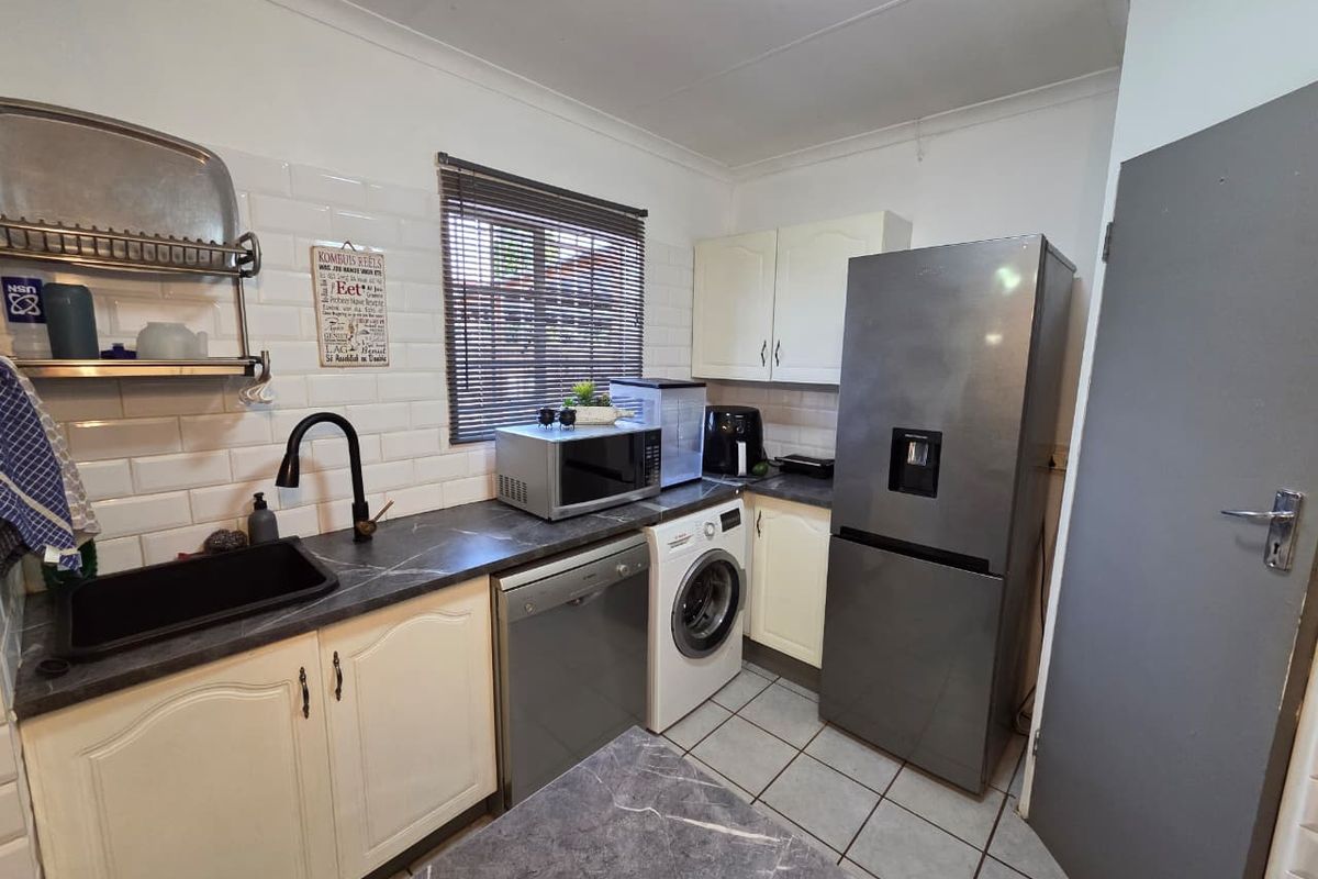 A functional kitchen featuring subway tile backsplash, dark laminate countertops, undermount sink with gooseneck faucet, and ample built-in cabinetry.