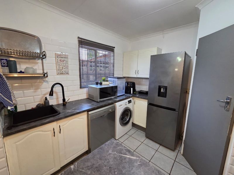 A functional kitchen featuring subway tile backsplash, dark laminate countertops, undermount sink with gooseneck faucet, and ample built-in cabinetry.