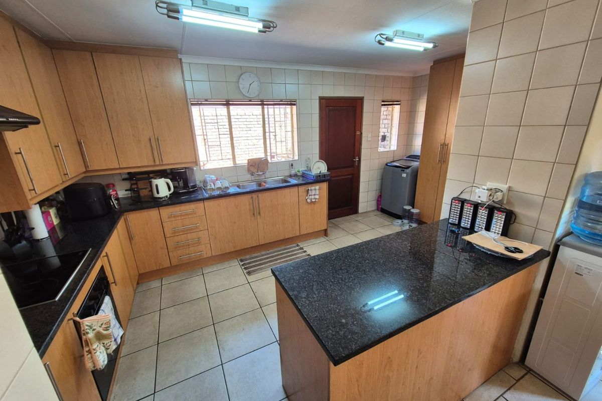 A functional kitchen featuring wood-finish cabinetry, granite countertops, a central island, and tiled flooring, offering a practical layout with integrated appliances.