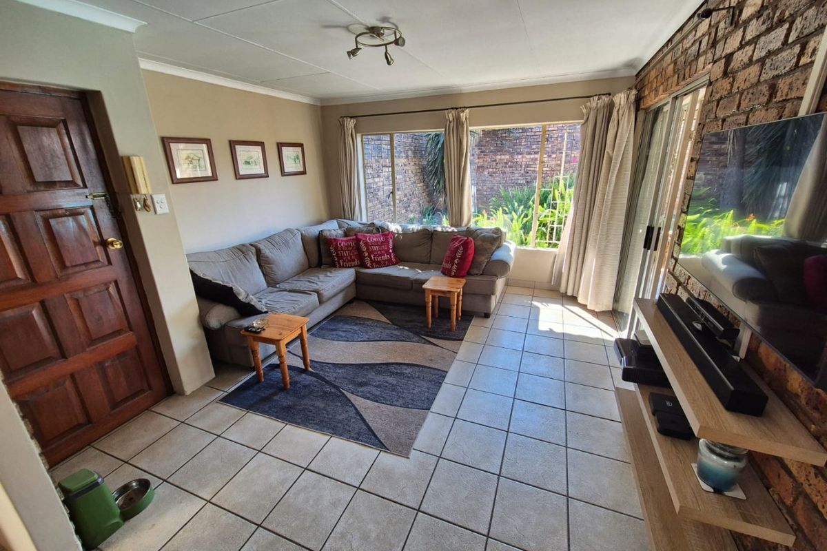 A comfortable living room featuring tiled flooring, an exposed brick feature wall, and large windows that provide natural light and garden views.