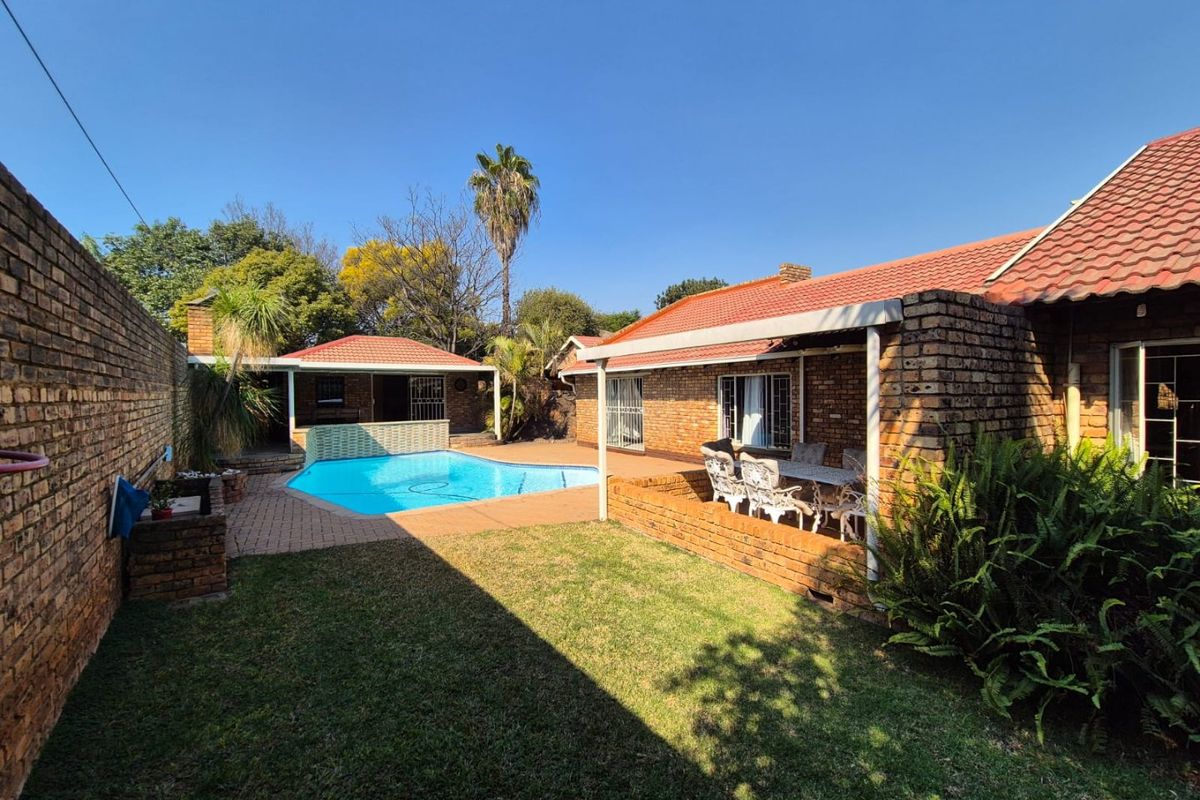 Rear garden area featuring a swimming pool, covered patio space, and established lawn, enclosed by brick boundary walls.