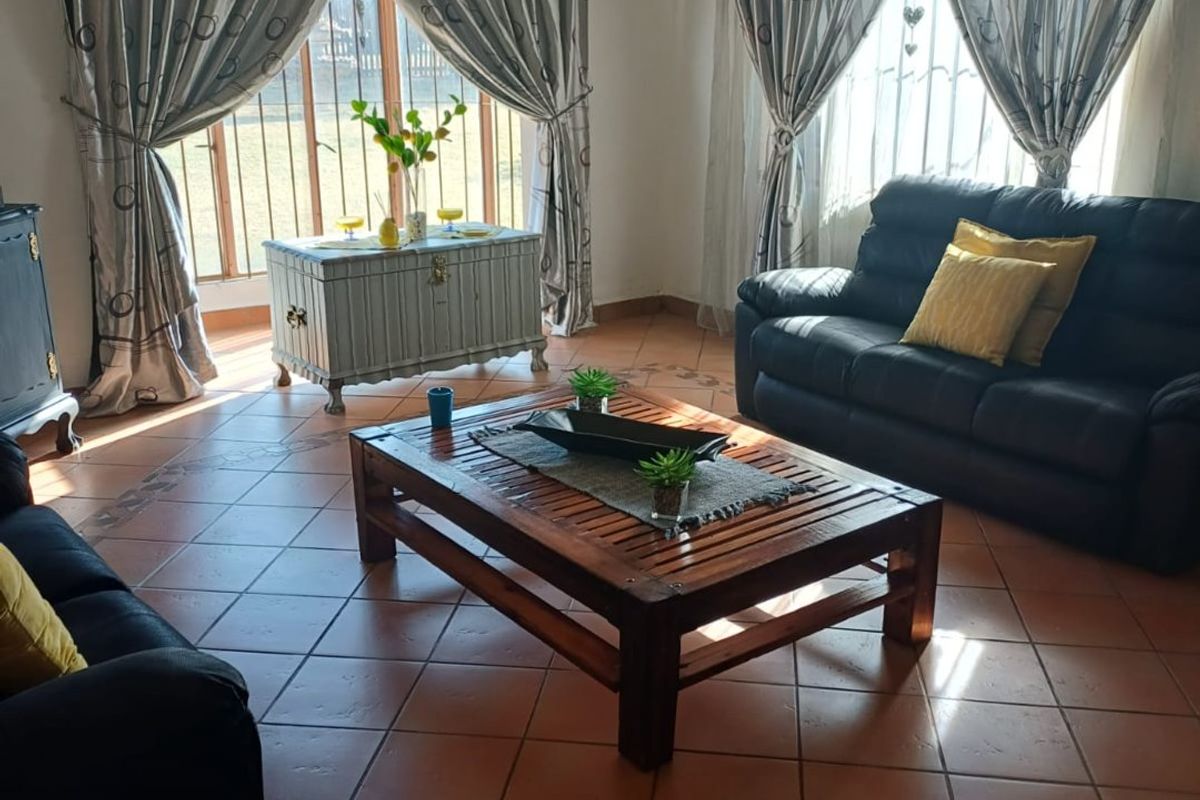 Spacious living room featuring terracotta floor tiles with decorative borders and large windows fitted with security bars, allowing for ample natural light.