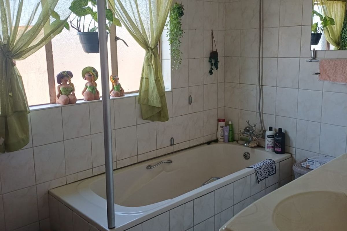 A functional bathroom featuring a built-in bathtub with shower attachment, tiled walls, and a vanity basin, offering potential for modernization.