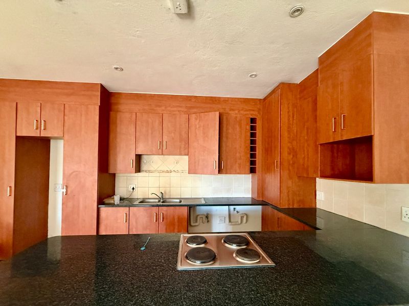 A dated kitchen featuring wooden cabinetry, granite countertops, and an integrated electric hob, currently requiring minor repairs and cosmetic updates.