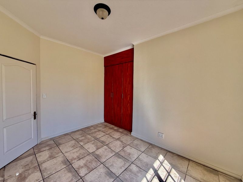 An empty bedroom featuring tiled flooring and built-in wooden cupboards, offering a blank canvas for personalization.