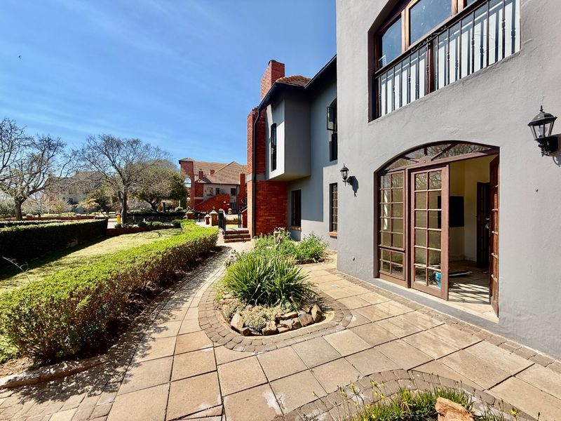Rear view of the property featuring a paved patio area, landscaped garden, and access to the interior through timber-framed glass doors.