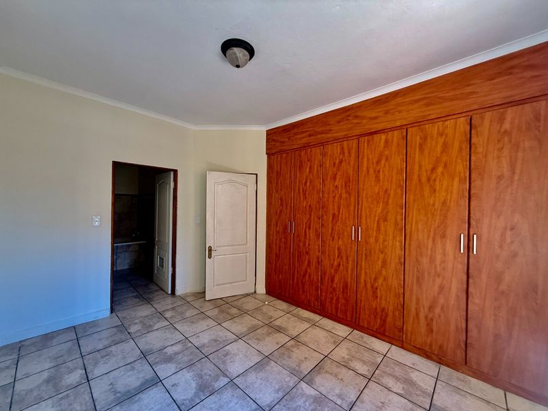 An empty bedroom featuring built-in wooden wardrobes, tiled flooring, and direct access to an adjoining bathroom.