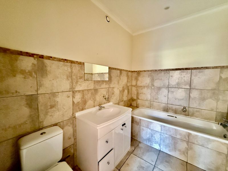 A functional bathroom featuring a vanity cabinet with basin, a standard bathtub, and a toilet, finished with neutral wall and floor tiling.