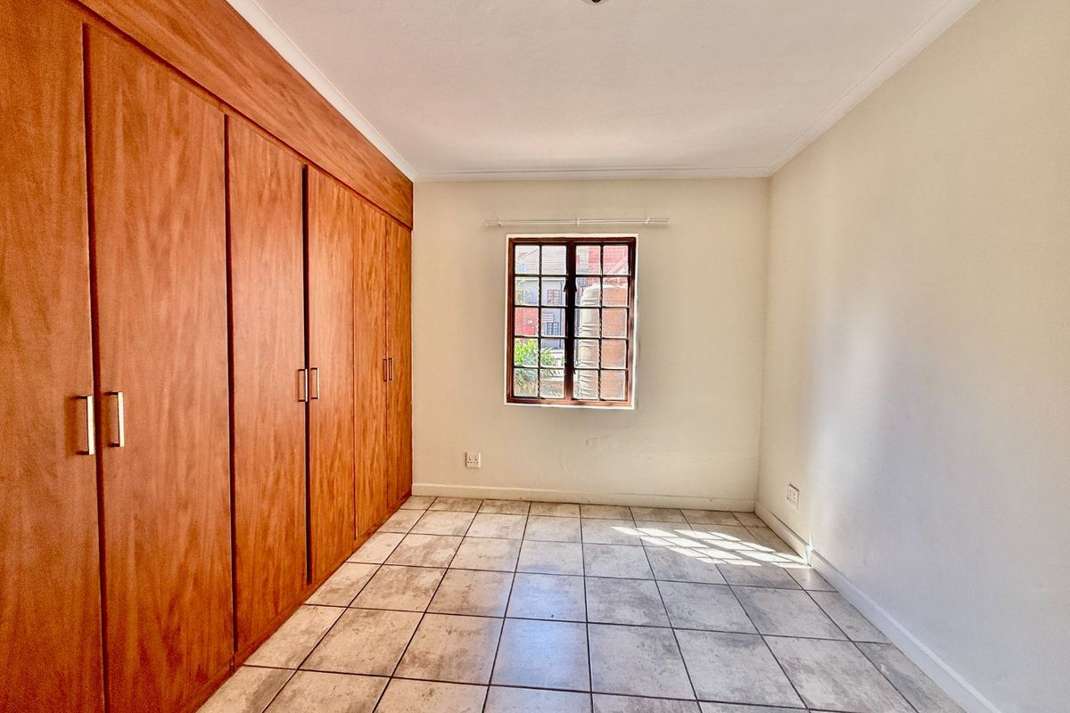 A bright, empty bedroom featuring tiled flooring and extensive built-in wooden cabinetry, offering ample storage space.