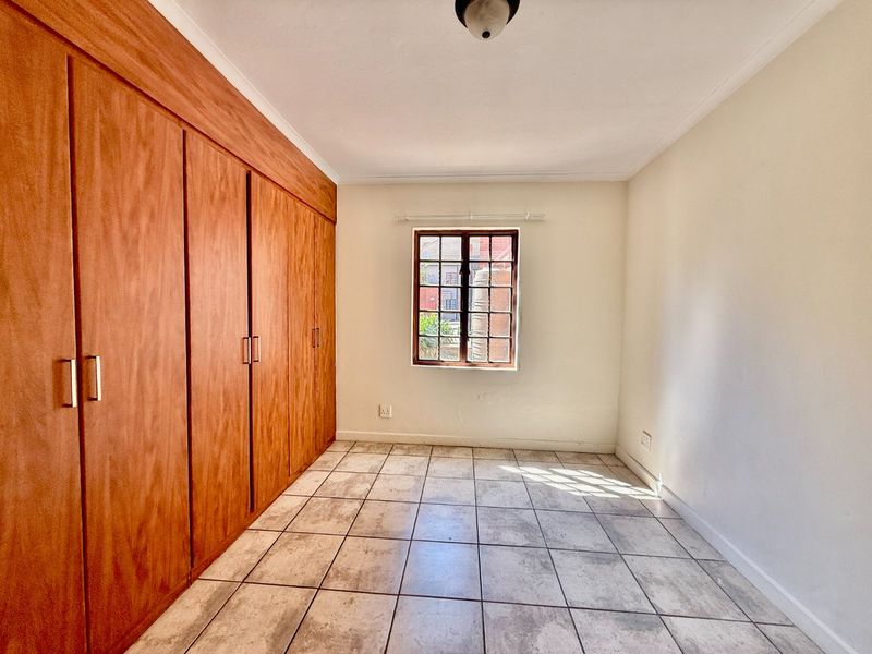 A bright, empty bedroom featuring tiled flooring and extensive built-in wooden cabinetry, offering ample storage space.