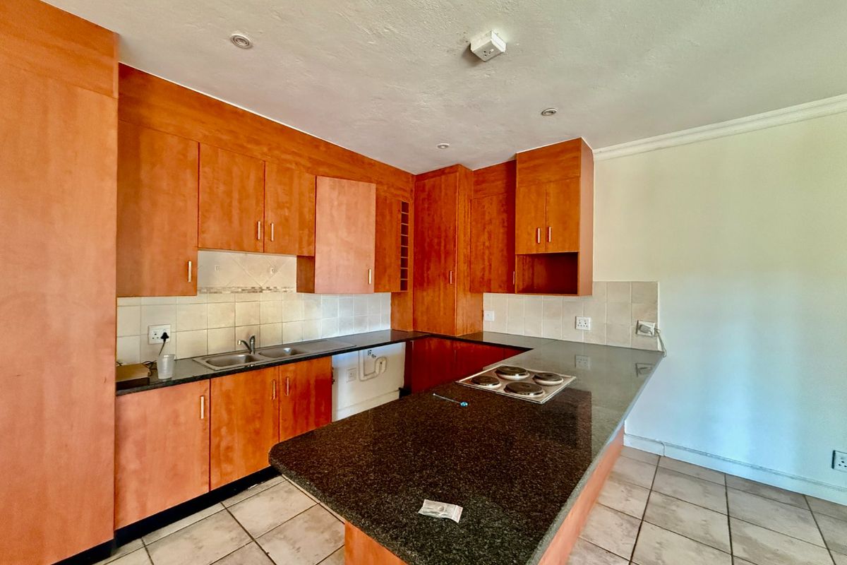 A functional kitchen featuring wooden cabinetry, granite countertops, an integrated electric hob, and tiled flooring, offering a practical layout for culinary activities.