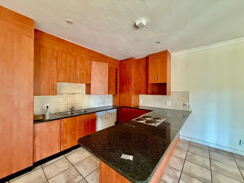 A functional kitchen featuring wooden cabinetry, granite countertops, an integrated electric hob, and tiled flooring, offering a practical layout for culinary activities.