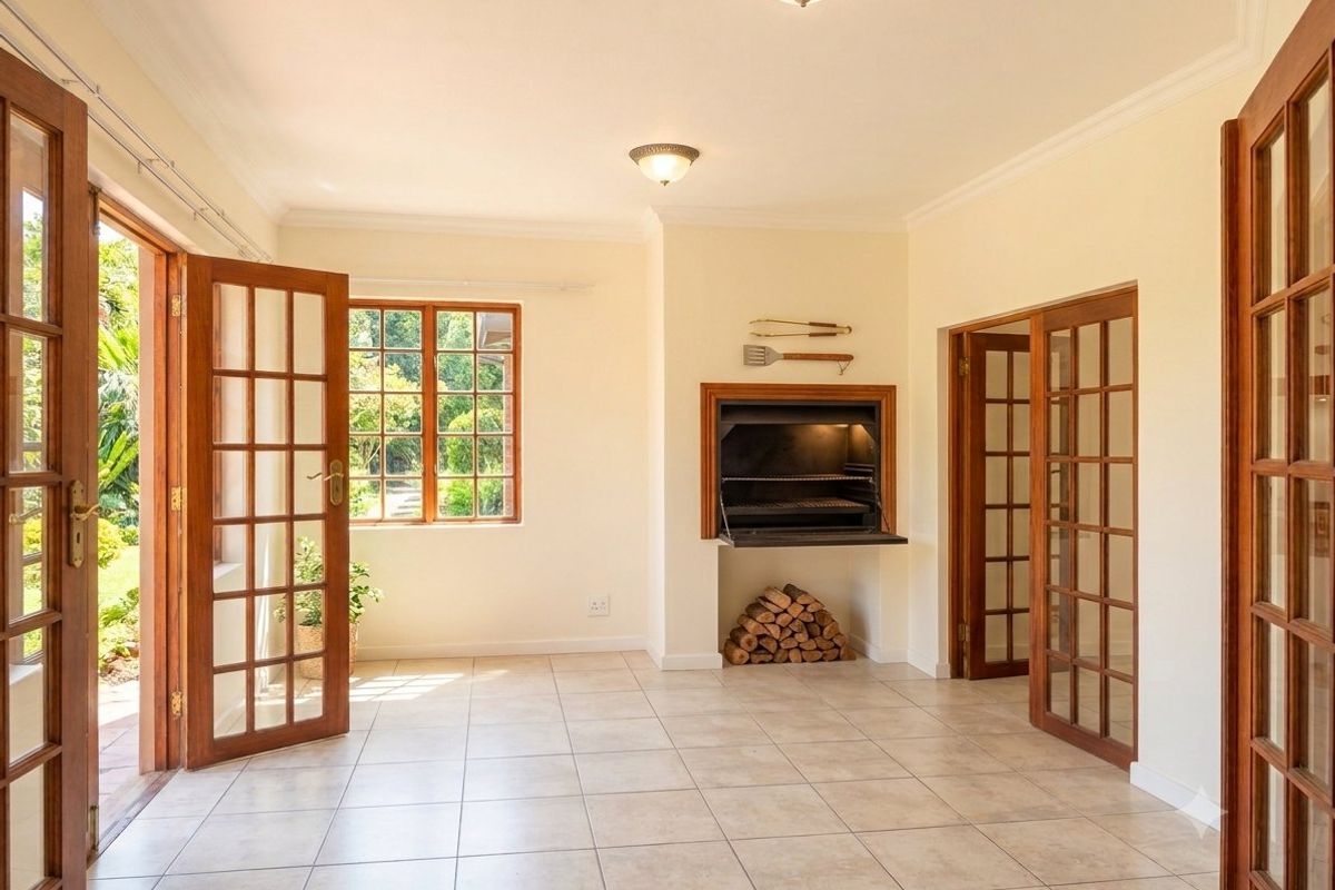 Spacious living area featuring tiled floors, classic wooden french doors, and a built-in indoor braai, offering direct access to the garden.
