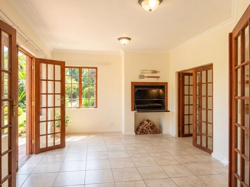 Spacious living area featuring tiled floors, classic wooden french doors, and a built-in indoor braai, offering direct access to the garden.