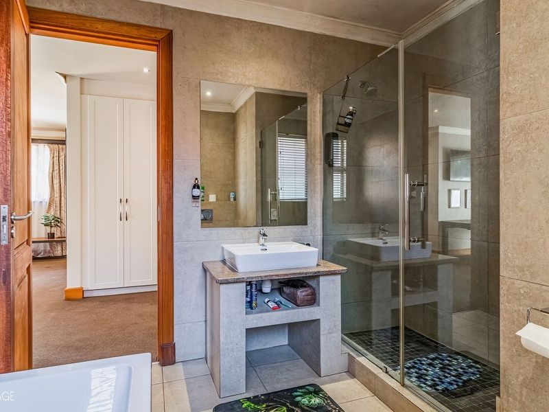 Modern bathroom featuring a glass-enclosed shower, stone-topped vanity with a vessel sink, and neutral wall tiling.