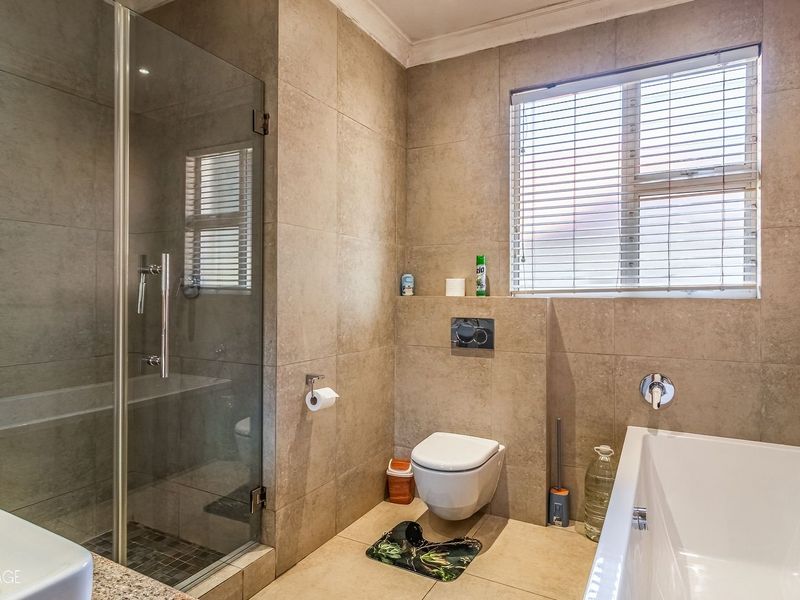 Modern bathroom featuring a glass-enclosed shower, a wall-mounted toilet, and a built-in bathtub with neutral floor-to-ceiling tiling.