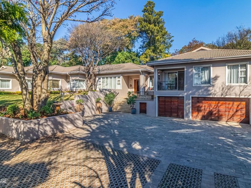 A well-maintained single-story residential property featuring a paved driveway, double garage, and an elevated balcony entrance set within a landscaped garden.