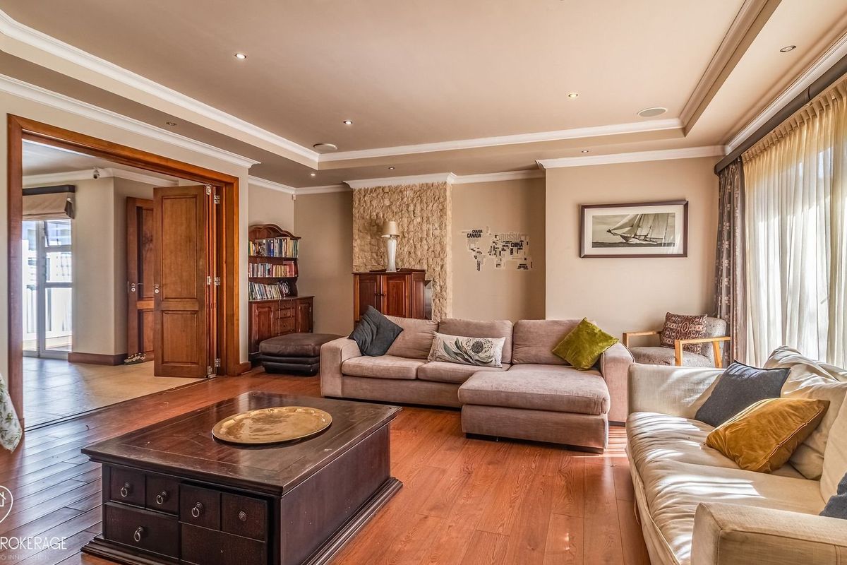 Spacious living room featuring hardwood flooring, recessed ceiling lighting, crown molding, and a distinctive stone feature wall, leading into an adjacent room.