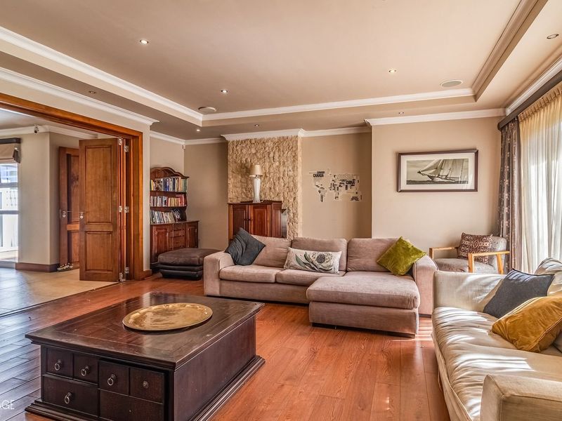 Spacious living room featuring hardwood flooring, recessed ceiling lighting, crown molding, and a distinctive stone feature wall, leading into an adjacent room.