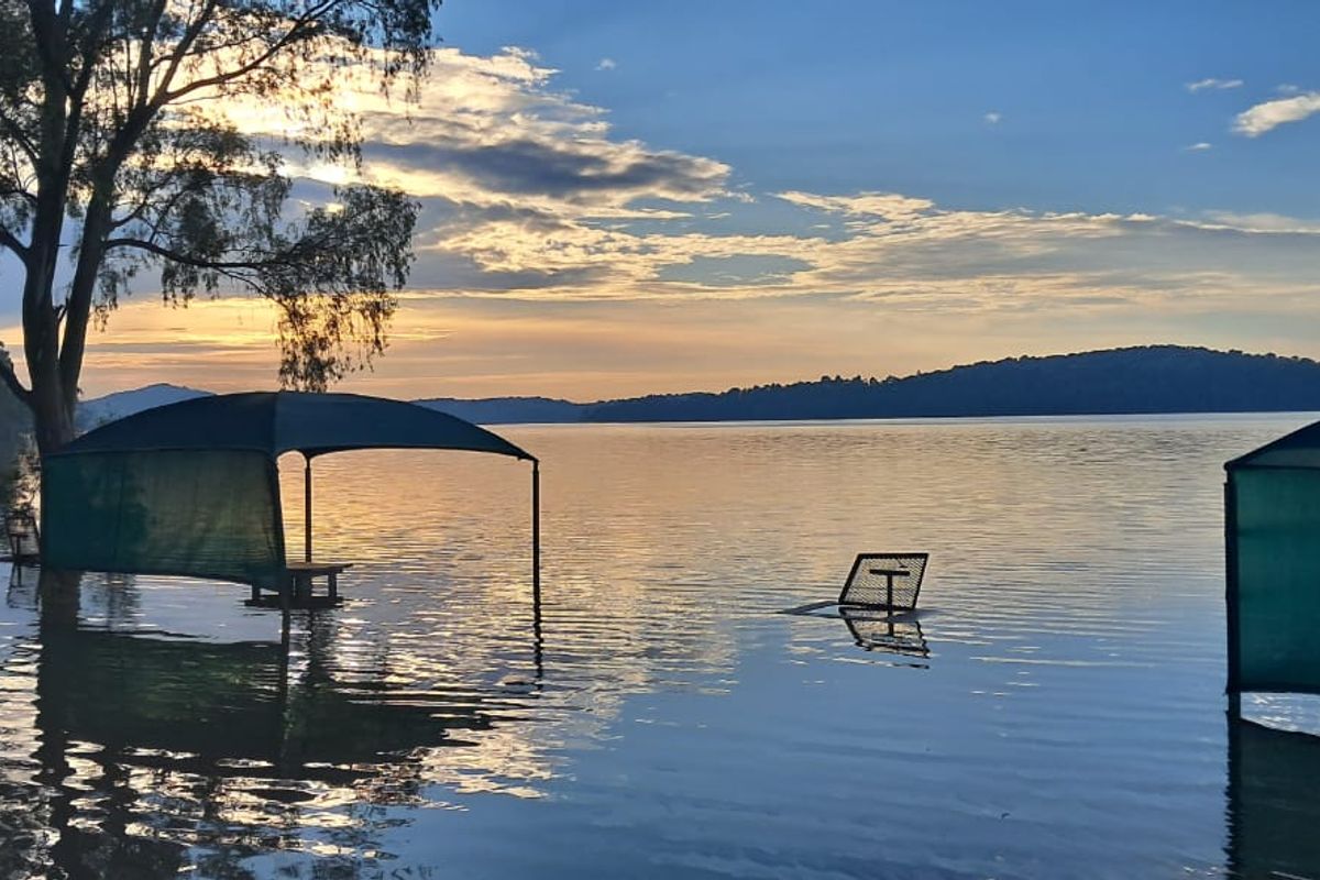 A scenic view of a lake at sunset, showing significant flooding affecting the shoreline and outdoor structures.