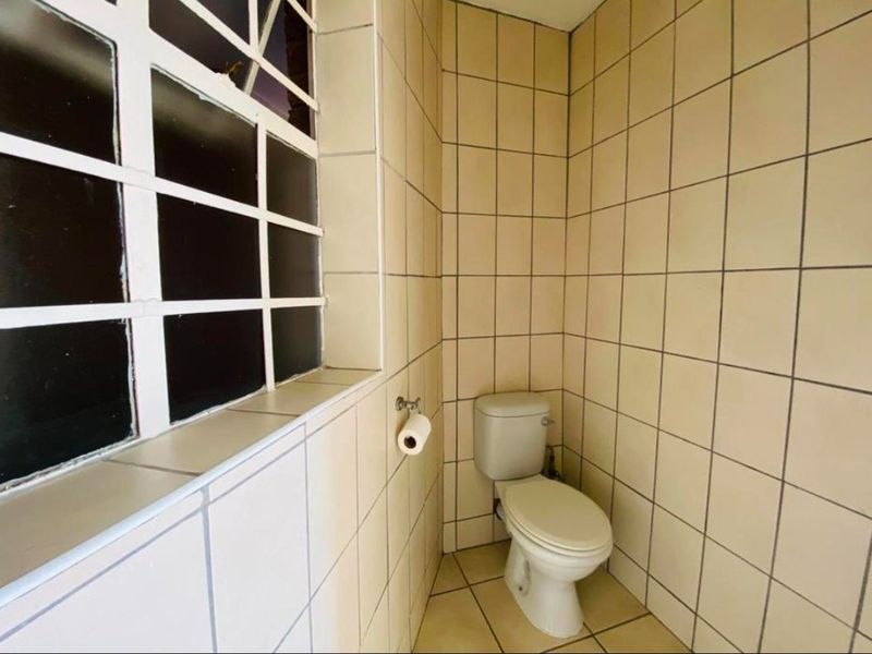 A compact bathroom featuring full-height ceramic wall tiling, tiled flooring, and a standard toilet suite with a window.