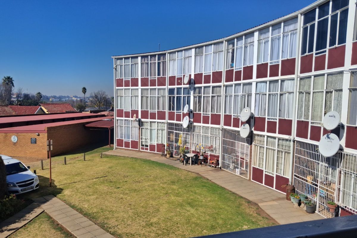 View of the rear apartment building facade featuring large windows, security bars, and communal lawn area with paved walkways.