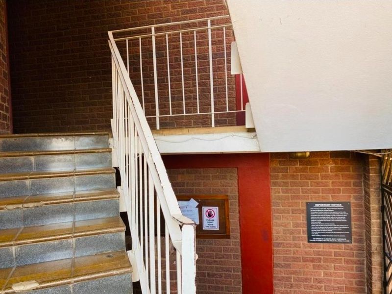 Exterior entrance area featuring a brick facade, tiled staircase, and metal balustrade leading to the apartment access point.