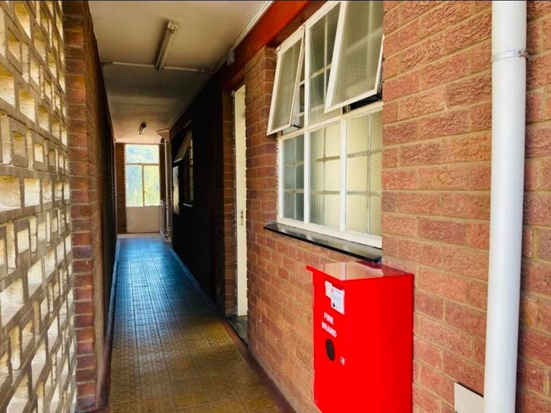 A functional apartment building hallway featuring exposed brick walls, tiled flooring, and a wall-mounted fire hose reel.