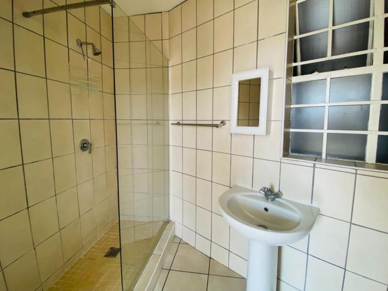 A functional bathroom featuring a glass-enclosed shower, pedestal basin, and tiled finishes, requiring some cosmetic updates to modernize the space.