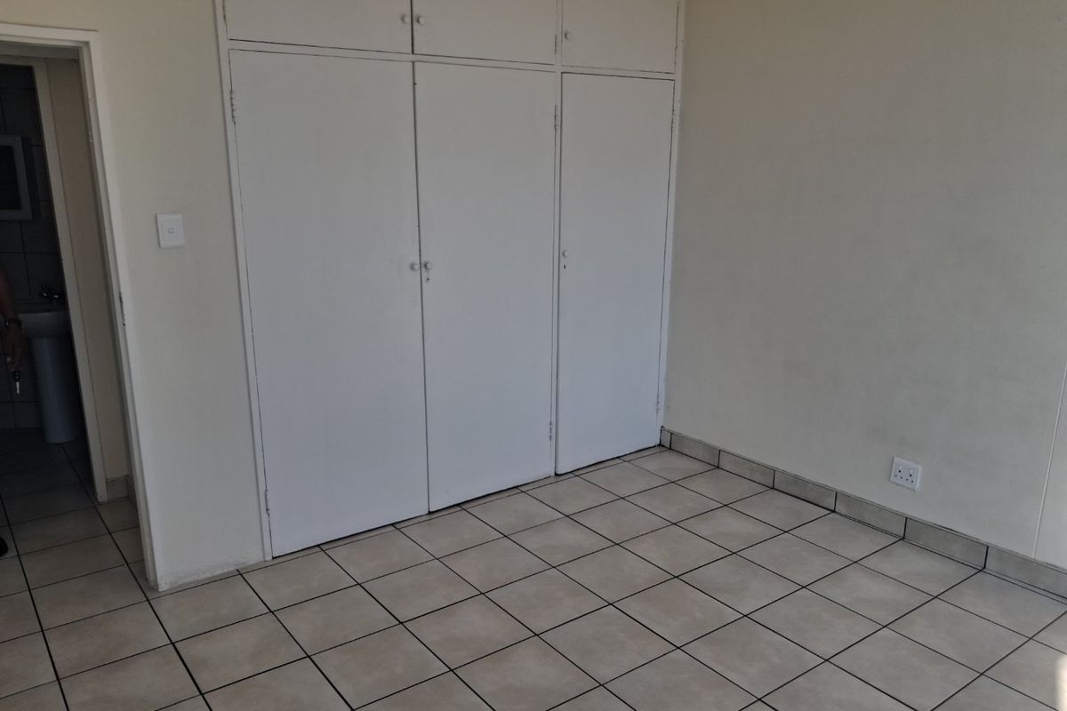 An empty bedroom featuring neutral tiled flooring and white built-in cupboards with overhead storage compartments.